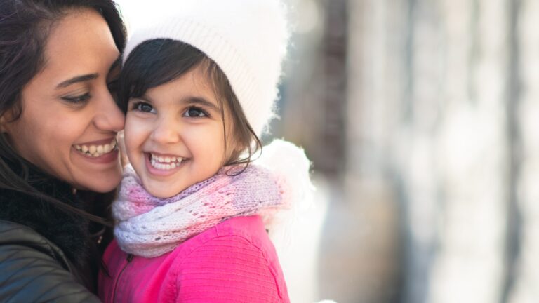 young mom holding and kissing toddler aged daughter on cheek