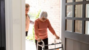 Elderly woman with a walker being helped inside her home.