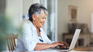 Older woman smiling while reading something on her laptop.